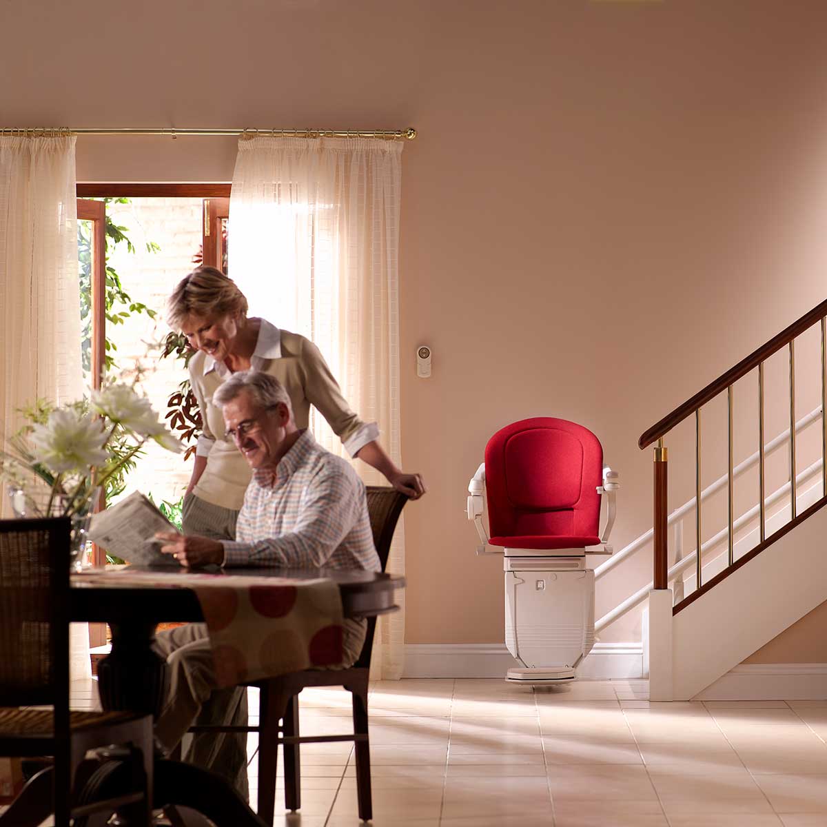 Ein älterer Mann sitzt an einem Tisch und liest eine Zeitung hinter ihm steht eine ältere Frau und sieht zu das Interieur eines warm beleuchteten Hauses verfügt über einen Sitzlift